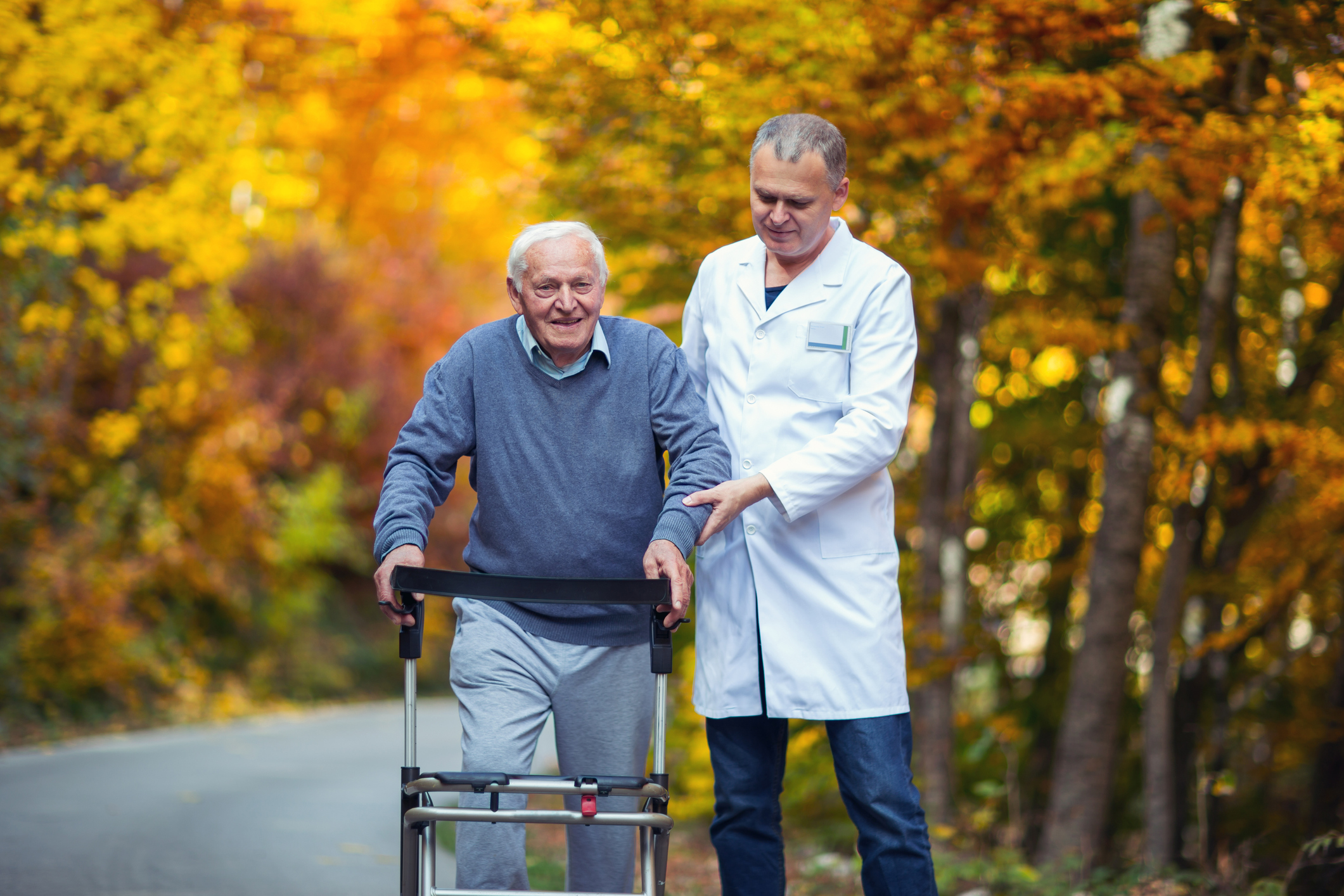 Male nurse assisting senior patient with walker outdoor