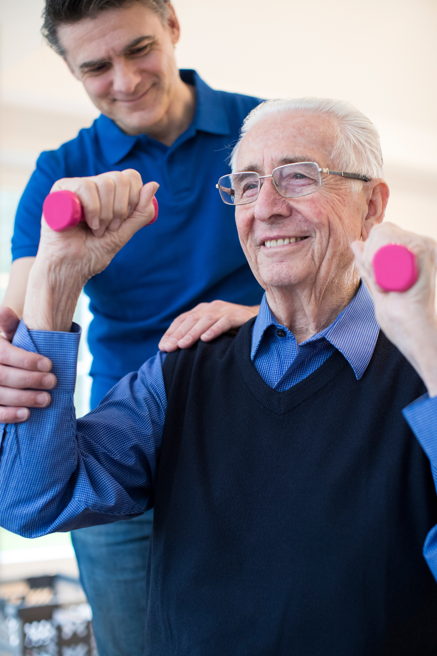 Physiotherapist Helping Senior Man To Lift Hand Weights